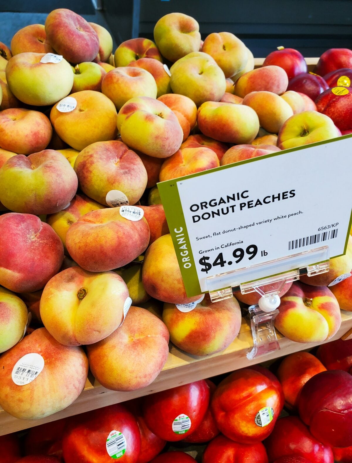 The image shows a cluster of organic donut peaches, also known as Saturn peaches, with their distinctive flat, round shape and dimpled centers. Their velvety skin ranges in color from pale pink to yellow with blush tones. Grown without synthetic pesticides or fertilizers, these peaches are known for their sweet, low-acid flavor and juicy texture. The photo captures the natural, farm-fresh quality of the fruit, ideal for showcasing seasonal produce or healthy eating themes.